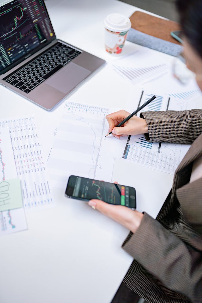 services-03 Adult woman analyzing stock market data with laptop and smartphone in office setting.